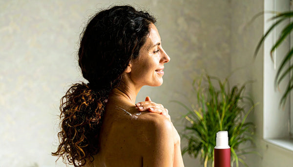 Person applying mineral sunscreen indoors near a window on a cloudy day, with a white pump bottle on the counter, illustrating year-round SPF protection.