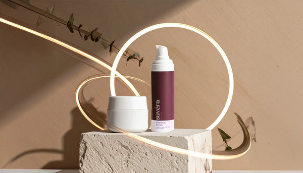 Minimalist flat lay of five neutral body-care products on warm beige linen, evoking inclusive, genderless self-care with a soft, hydration-first aesthetic.