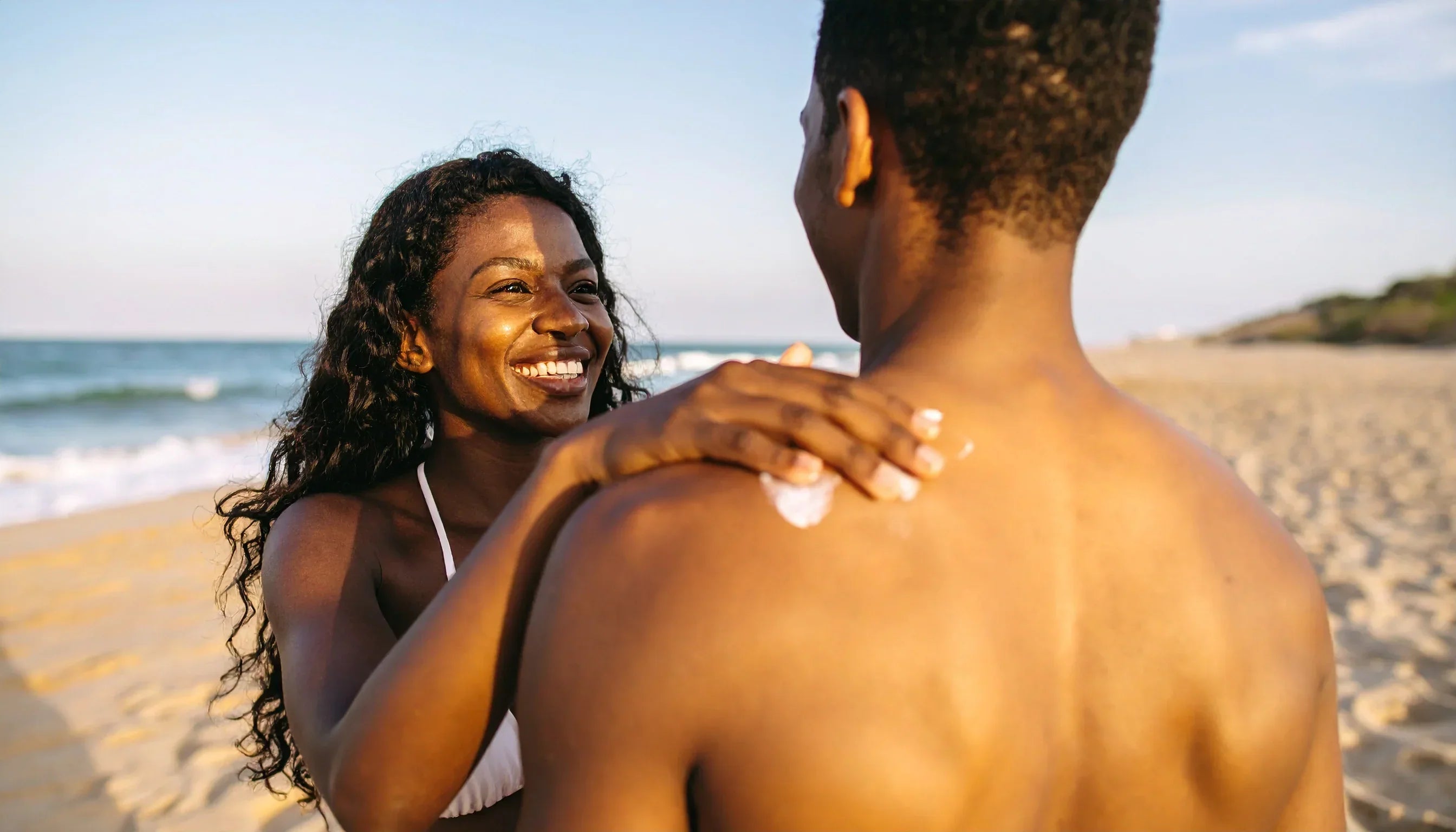 Adult woman applying Suvéra mineral sunscreen SPF30 on man’s shoulder at the beach – vegan sun care, natural skin protection, clean beauty.