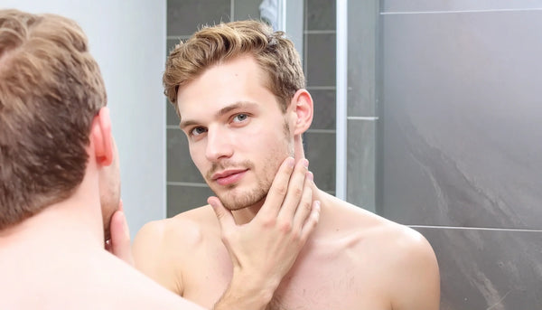 Man checking his face in the mirror after applying skincare, demonstrating a clean and matte complexion in a modern bathroom