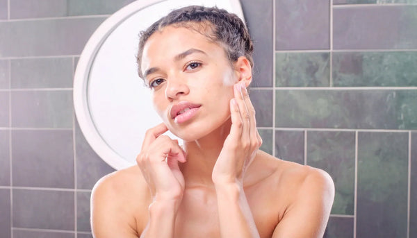 Woman with oily skin gently touching her face in a modern bathroom.