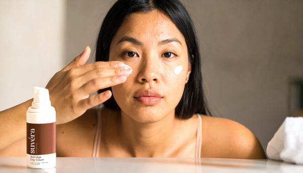 Photoreal hero image of a woman in a minimal bathroom applying too much skincare at once, with visible cream smear and serum drops to illustrate common routine mistakes.