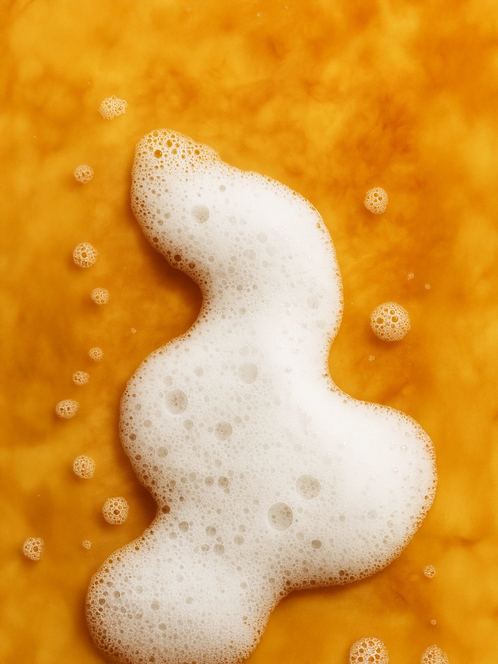 Foamy white substance on a textured orange surface Foamy white lather on warm amber stone, evoking Patchouli & Amber Vanilla hand and body wash by Suvéra—clean, cozy, natural skincare.