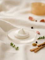 White cream on a clear plate with cinnamon sticks and herbs on a white cloth background Suvéra Self Care body serum—silky white dollop on a clear glass dish over soft cream cloth, eye-level, airy lighting.