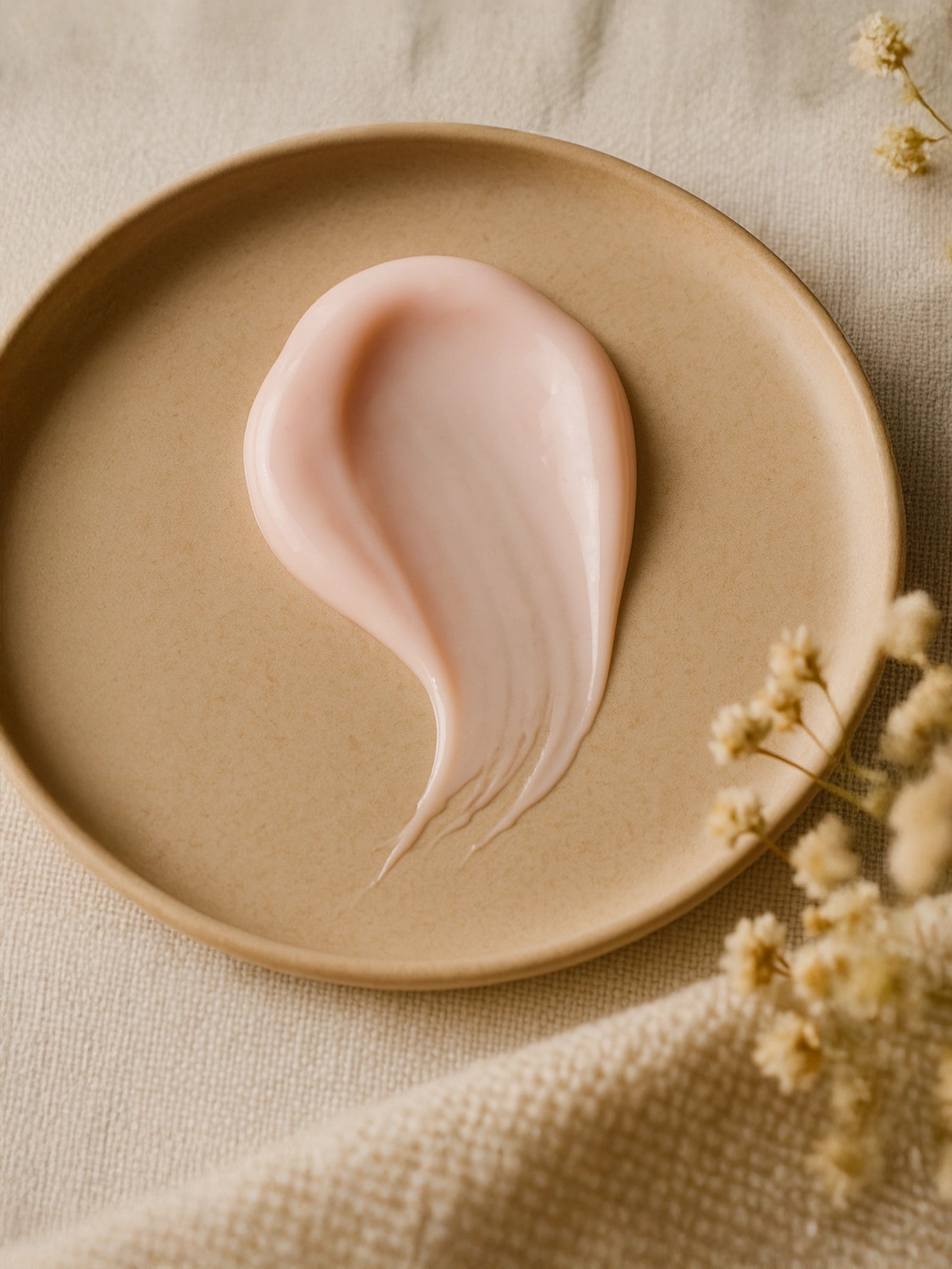 Pink cream on a beige plate with dried flowers on a beige fabric background Hydrating Serum