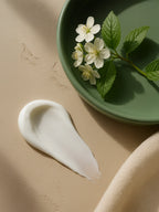 White cream smear with a green plate holding flowers and leaves on a beige background Moisturising Day Cream
