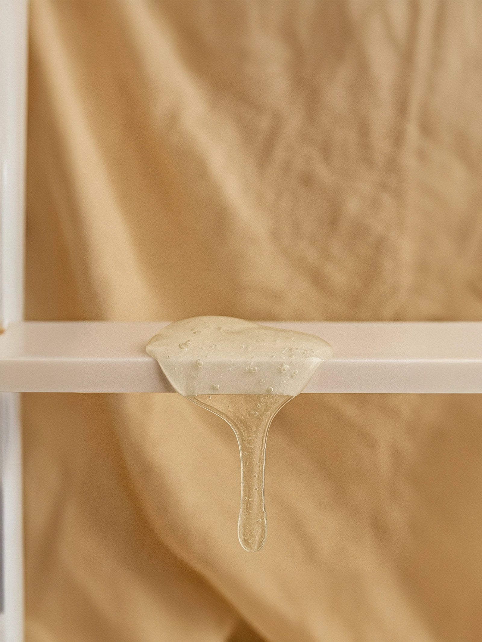 Beige fabric with a small amount of beige liquid on a white shelf against a beige background Close-up of clear, glossy shampoo texture with soft ripples and air bubbles on a smooth surface — Suvéra Moisturising Shampoo for natural self-care