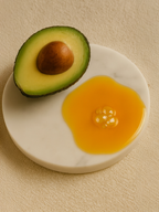 Half of an avocado on a white plate with a yellow fruit on a beige background Nourishing Facial Oil

