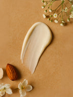 Cream swatch on a brown background with flowers and an almond Pigment Perfecting Serum
