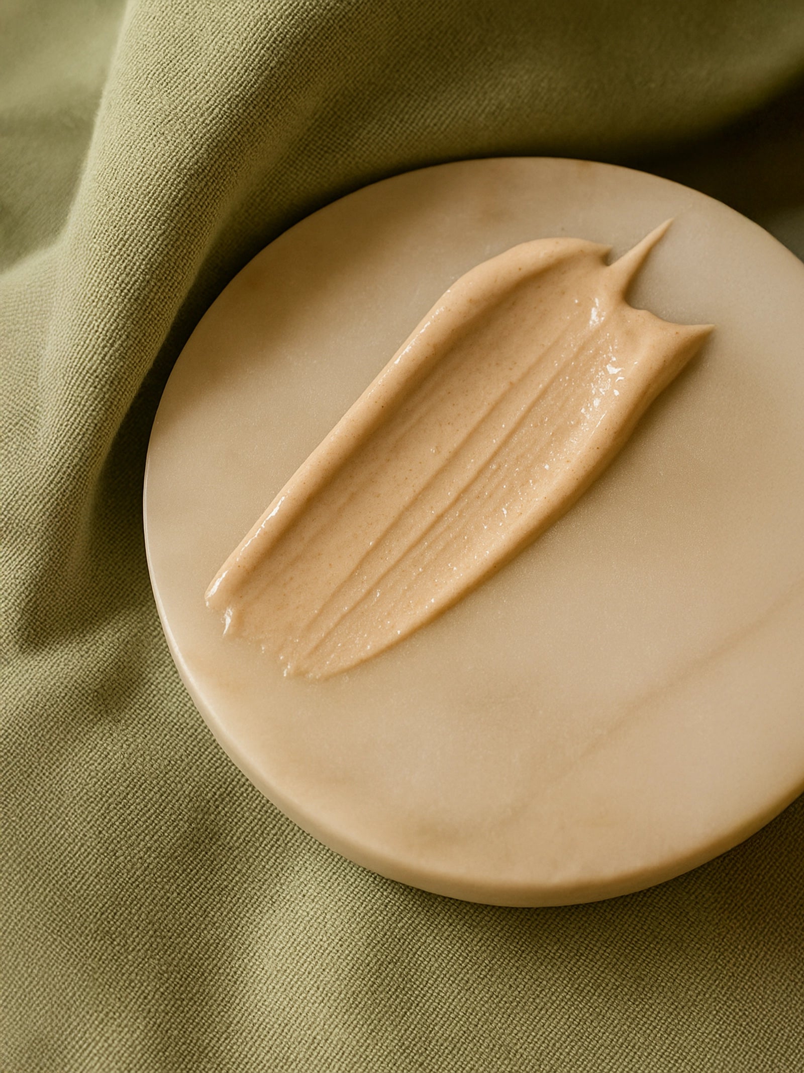 Beige cream on a round beige plate with a green fabric background Sunscreen SPF30, with tint