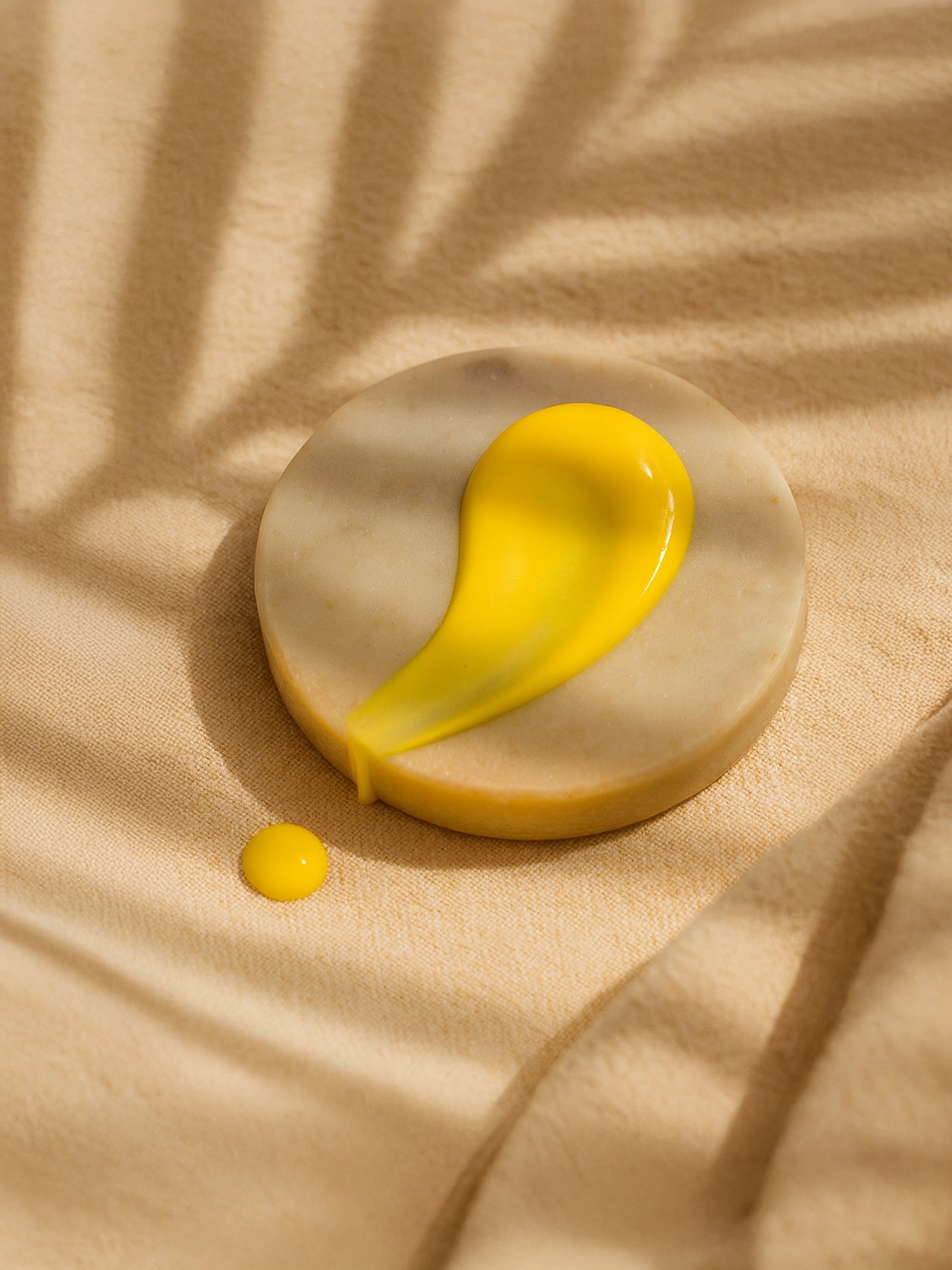 Yellow liquid droplet on a beige stone surface with a soft shadow Vitamin C Serum