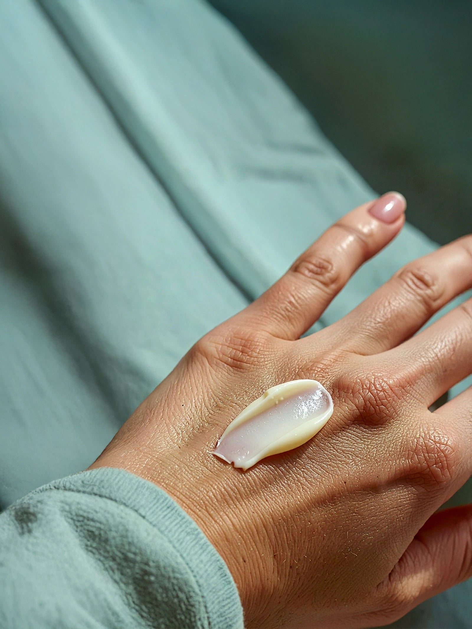 Hand with a small white object on a blurred green background A smooth layer of Suvéra Anti-Age Day Cream applied to the back of a hand, showing its rich yet silky texture under soft natural light.