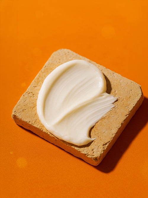 Beige bar of soap with white cream on an orange background