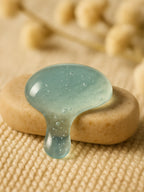 Clear gel-like substance on a textured beige surface with blurred natural elements in the background