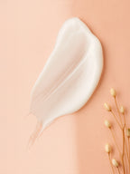 White cream smear on a beige background with dried flowers Creamy white droplet on a beige fabric background with a small yellow flower. Close-up of skincare serum drops beside champagne silk fabric and dried flowers on a neutral backdrop