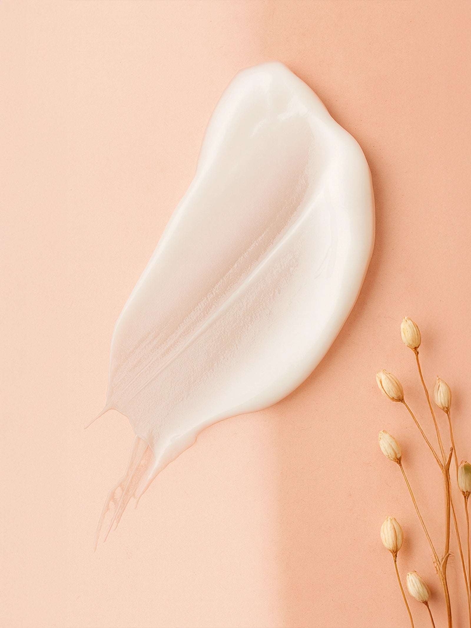 White cream smear on a beige background with dried flowers Creamy white droplet on a beige fabric background with a small yellow flower. Close-up of skincare serum drops beside champagne silk fabric and dried flowers on a neutral backdrop