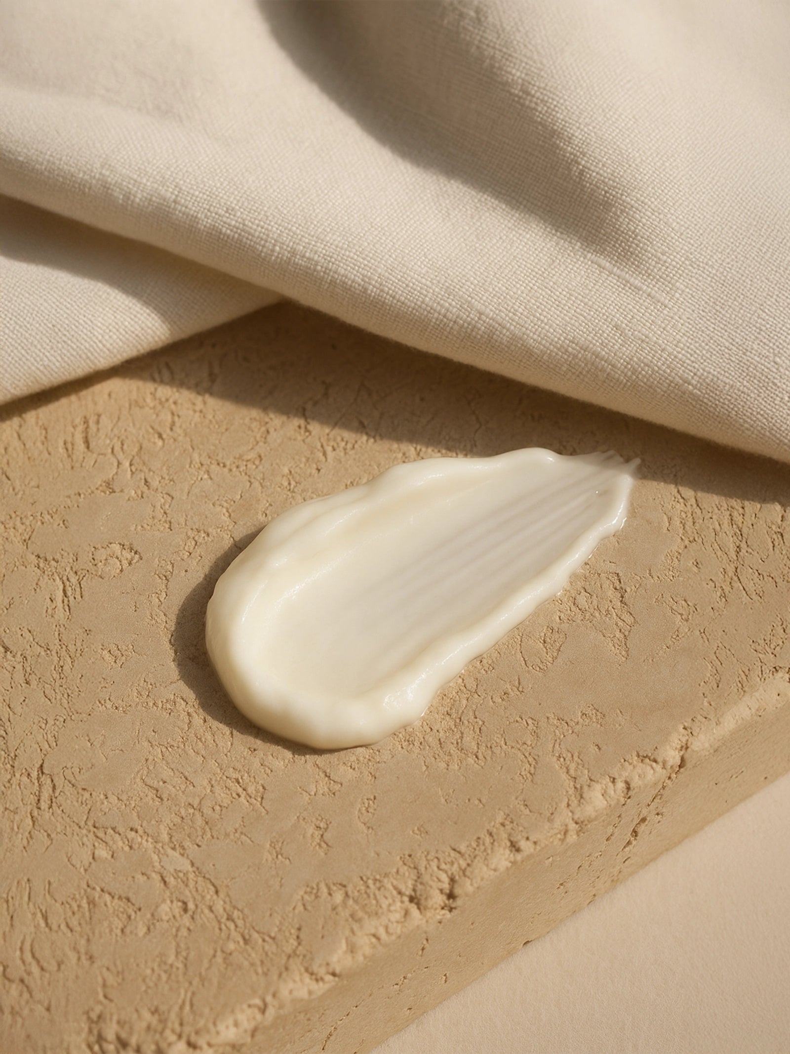 Beige cream smear on a textured beige surface with fabric in the background