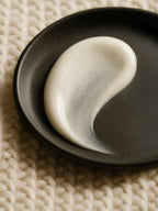 White cream on a black plate on a textured beige surface cleansing milk natural skincare