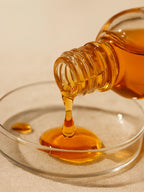Honey being poured from a bottle into a clear dish on a beige background