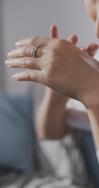 Hyperreal close-up of creamy lotion resting on forearm; out-of-focus botanicals suggest woody amber and leather notes.
