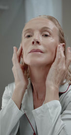 Mature lady in late 50s applying soothing pigment serum oil cream to her face natural COSMOS
